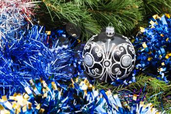 Christmas still life - one black glass Christmas bauble, blue tinsel on Xmas tree background