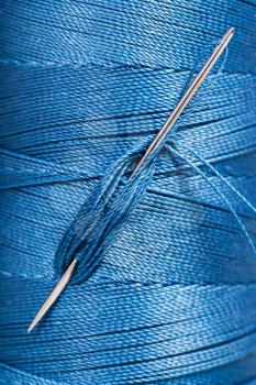 sewing needle in blue thread spool close up