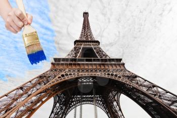 travel concept - hand with paintbrush paints blue sky over Eiffel tower in Paris city, France