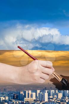 nature concept - seasons and weather changing: hand with paintbrush paints smog sky over blue city