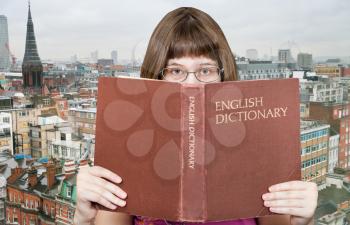 girl with spectacles looks over English Dictionary book and London skyline on background