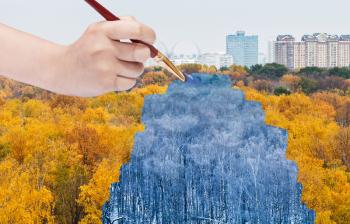 nature concept - seasons and weather changing: hand with paintbrush paints blue winter forest from yellow autumn forest