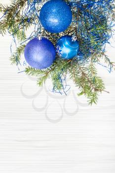 Christmas greeting card - border from three blue and violet Xmas baubles and tree branch on blank paper background