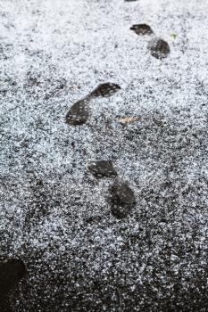 human footprints on sidewalk covered by first snow in autumn