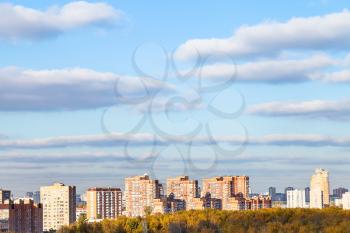 blue sky with clouds over modern apartment houses and yellow woods in sunny autumn day