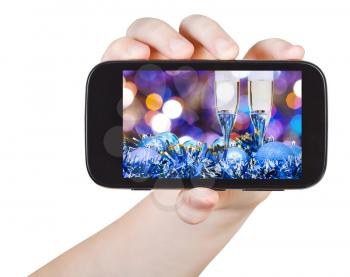 hand holds smartphone with Christmas still life on screen isolated on white background