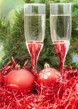 Christmas still life - Two glasses of sparkling wine with red Xmas baubles and tinsel on Christmas tree background