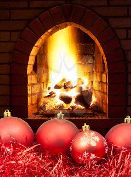 red Christmas balls and tinsel with open fire in home fireplace