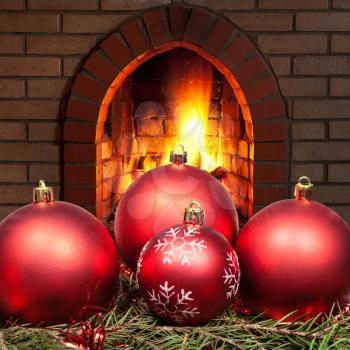 red Xmas baubles on green spruce tree with open fire in home fireplace