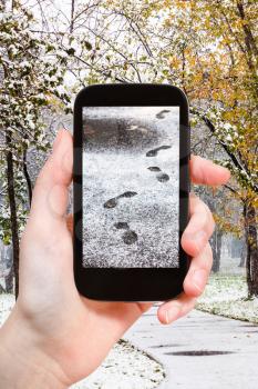 season concept - man taking picture of footprints of steps in first snow in city park on smartphone