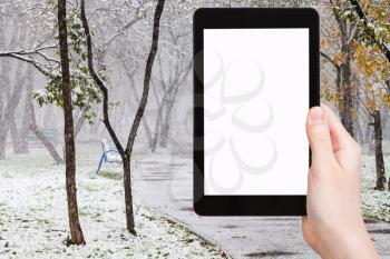 season concept - hand holds tablet pc with cut out screen and first snowfall in public garden on background