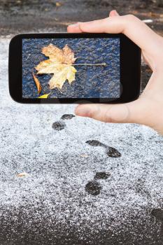 season concept - man taking picture of frozen fallen leaf in first snow on smartphone