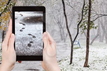 season concept - man taking picture of footprints of steps in first snow in urban park on tablet pc