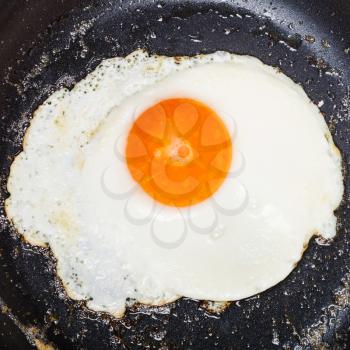 top view of one fried egg in black frypan close up