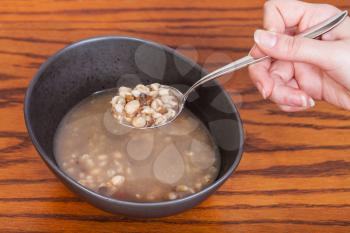 hand holds tablespoon with beans soup over ceramic bowl on wooden table