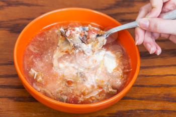 spoon with cabbage soup with sour cream in hand over ceramic bowl on wooden table