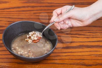 hand holding spoon with beans soup over ceramic bowl on wooden table