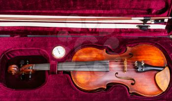 top view of old wooden violin with bow in red velvet case