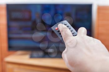 Hand turns on News on TV by remote control in living room