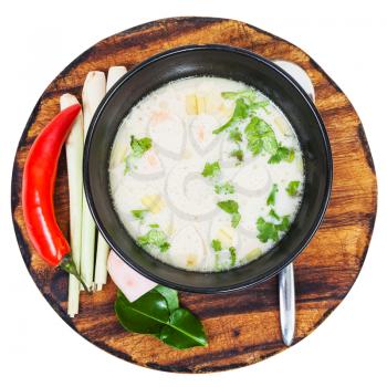 above view soup Tom yam nam khon made with shrimps, coconut milk, chilli pepper, lemongrass, galangal, coriander, kaffir lime leaves in bowl and ingredients on wood board isolated on white background