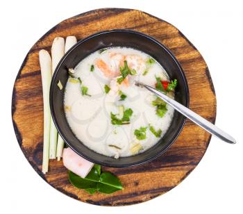 top view soup Tom yam nam khon made with shrimps, coconut milk, chilli pepper, lemongrass, galangal, coriander, kaffir lime leaves in bowl and ingredients on wooden board isolated on white background