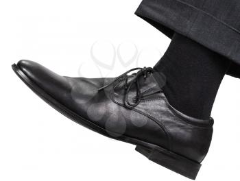 side view of male left leg in black shoe takes a step isolated on white background