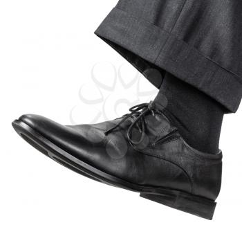side view of male left foot in black shoe takes a step isolated on white background
