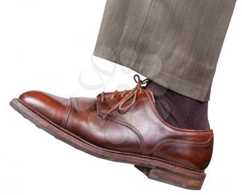 side view of male left leg in brown shoe takes a step isolated on white background