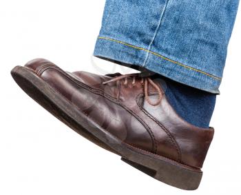 side view of male left leg in jeans and brown shoe takes a step isolated on white background