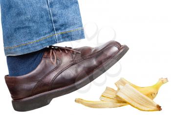 male right leg in jeans and brown shoe slips on a banana peel isolated on white background