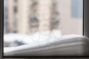 snow on window pane and houses on background in cold winter day