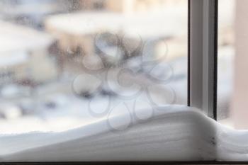 snowdrift on home windowpane and cityscape on background in sunny winter day