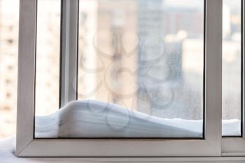 snowdrift on window casement and cityscape on background in sunny winter day