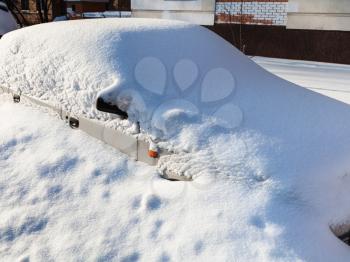 white car under snowdrift in parking lot near apartment house