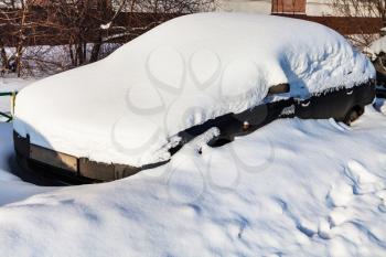 black car under fresh snow in parking lot near city house