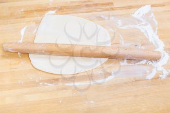 flour, rolling pin and rolled dough on wooden table