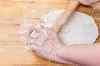 woman rolls out the dough with a rolling pin on wooden table