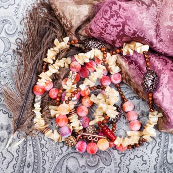 top view of tangled pink and yellow necklace from natural gemstones (pink Agate Dragon veins, horn, shell, mahogany obsidian beads and carved copper balls) on textile background