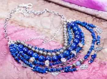 blue necklace from natural gem stones (lapis lazuli - lazurite, pyrite , glass lampwork beads) on painted textile background