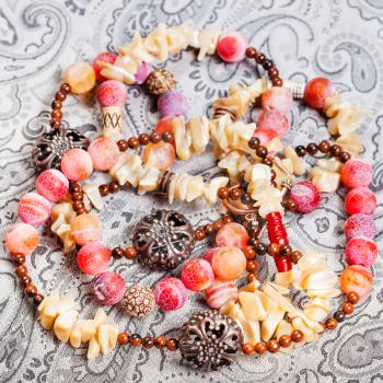 above view of tangled pink and yellow necklace from natural gemstones (pink Agate Dragon veins, horn, shell, mahogany obsidian beads and carved copper balls) on textile background