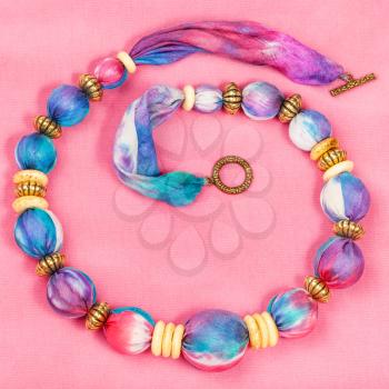 top view of textile necklace from pink and blue painted silk balls and brass and bone rings on pink background
