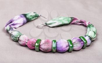 textile necklace from painted violet silk batik balls and green ceramic rings on gray background
