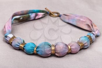 textile necklace from pink and blue painted silk and bronze beads on gray background