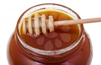 wooden stick on glass jar with brown honey close up isolated on white background