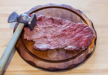 meat tenderizer and beaten slice of veal on cutting board