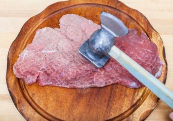 piece of veal is beating by meat mallet on cutting board