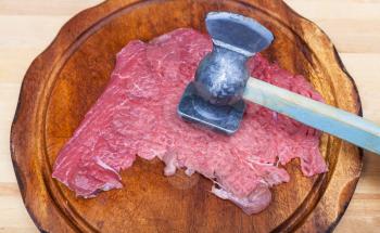 slice of veal is beating by meat tenderizer on cutting board