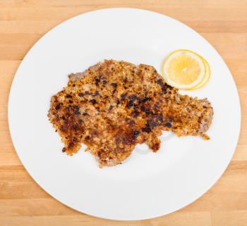 above view of fried veal schnitzel and lemon slices on white plate on wooden table