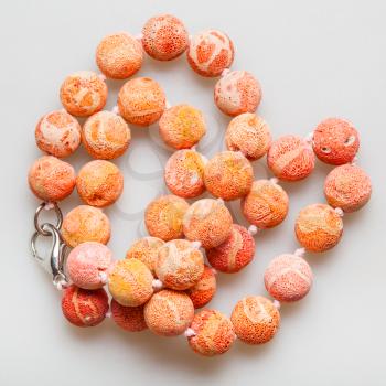 tangled necklace from orange sponge coral beads on gray background