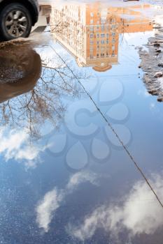 car and puddle from melting snow on street with reflection of urban house in sunny spring day